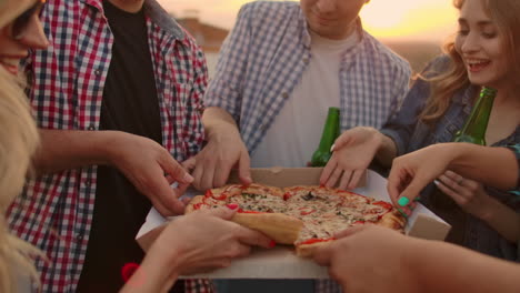 Eine-Gruppe-Von-Sechs-Jungen-Leuten-Verteilt-Heiße-Pizzastücke-Und-Isst-Sie-Gemeinsam.-Dies-Ist-Eine-Dachparty-Mit-Bier.